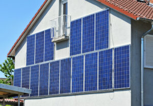 Sechszehn blaue Solarpanels an der Seite einer weißen Häuserfassade
